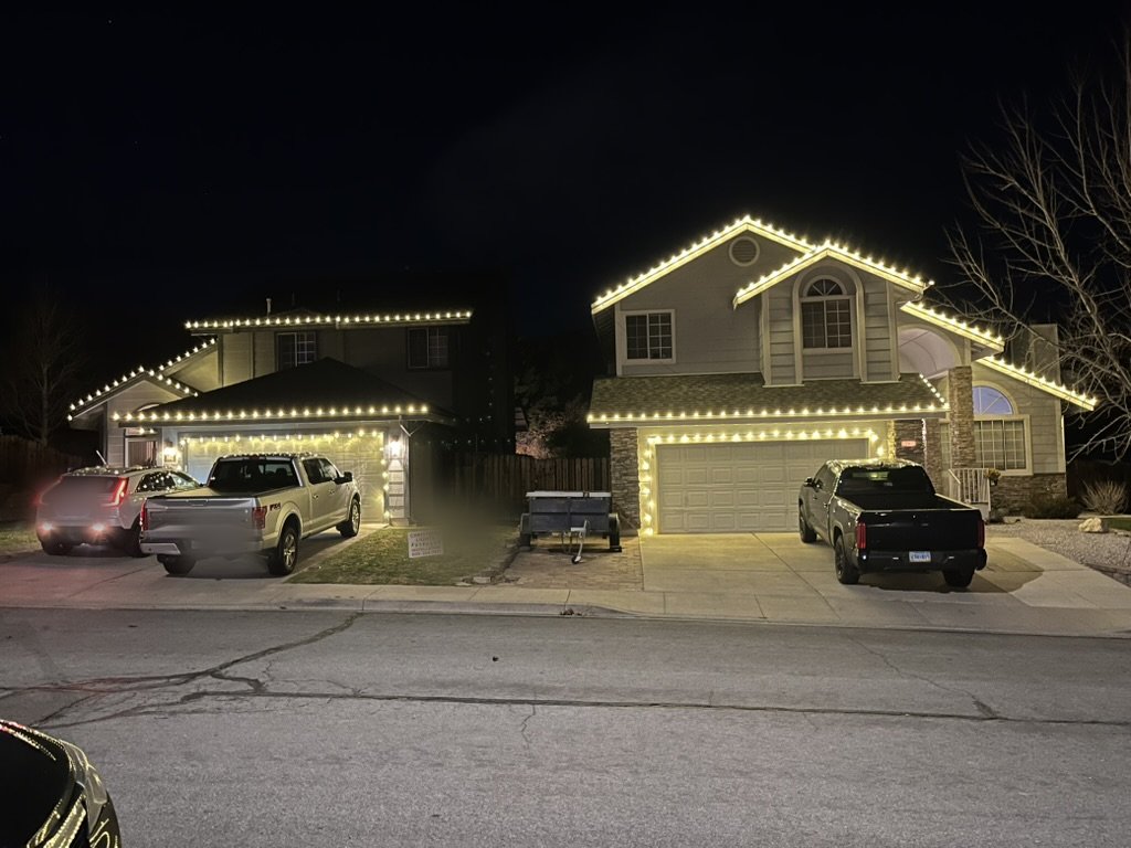 Warm white Christmas lights outlining the peaks and roofline of a two-story home at night