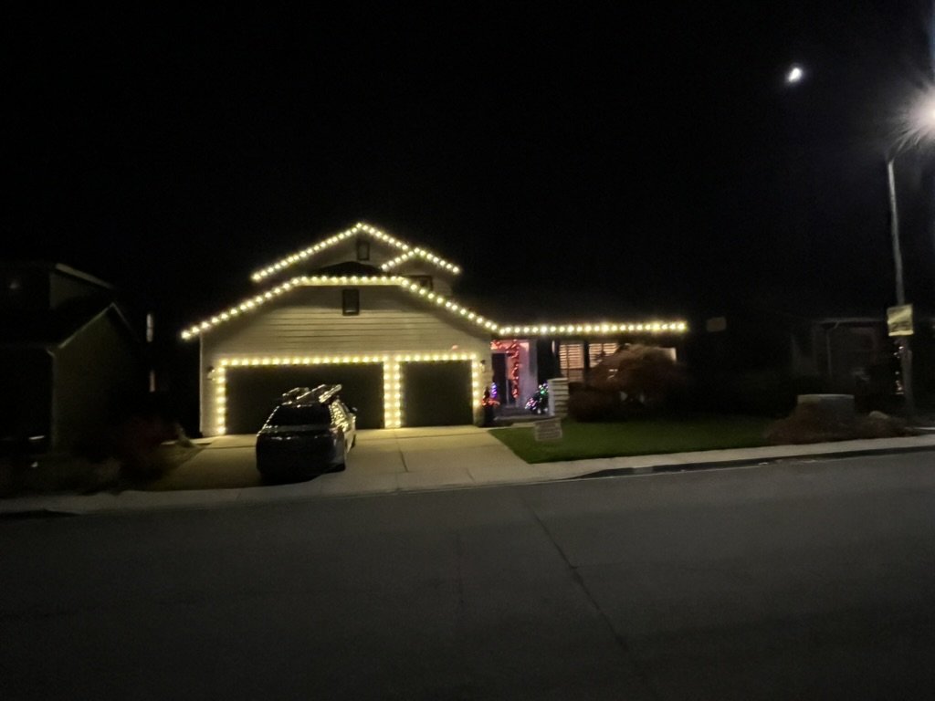 The same two-story home at night with warm white Christmas lights installed along the roofline